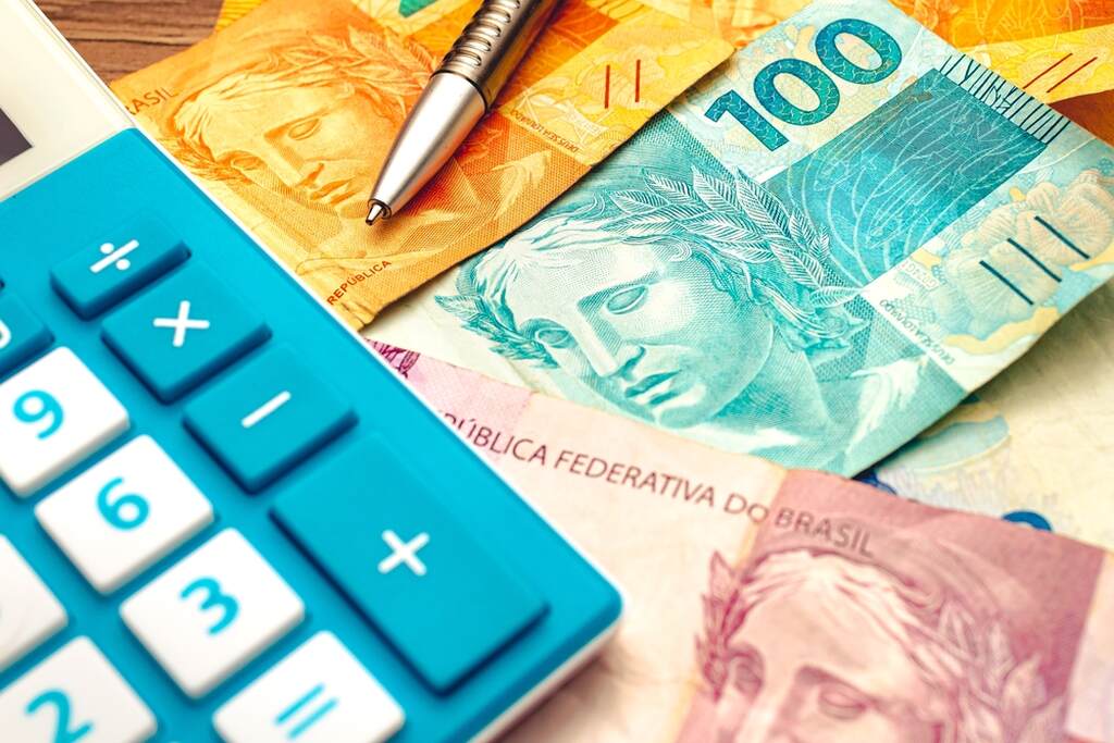 notas de reais brasileiras de diferentes valores (R$ 2, R$ 10, R$ 50 e R$ 100) junto com uma calculadora azul e uma caneta prateada