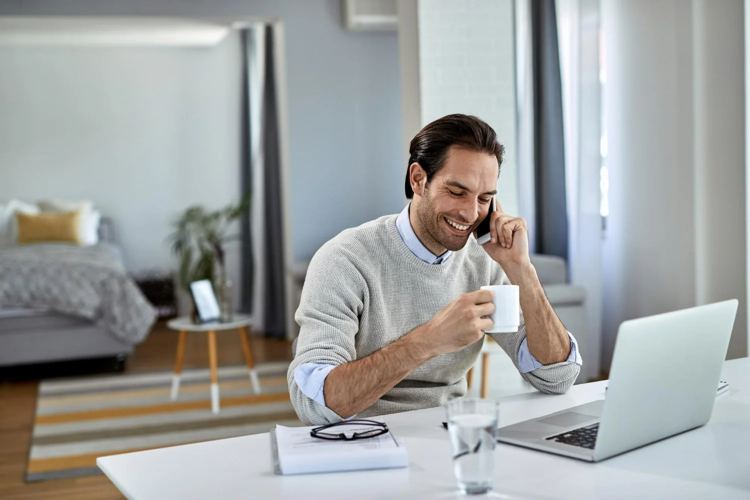 Profissional bebendo café enquanto se comunica pelo celular e realiza seu trabalho remoto no exterior